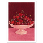 Red and burgundy cherries in a pale pink pedestal bowl on a pink tabletop against a deep red painted background.