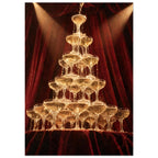 Champagne cascading down a tower of coupe glasses, lit by warm spotlights against deep burgundy curtains.