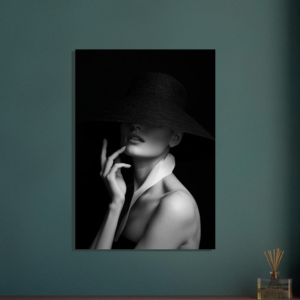 Woman in a wide-brim black hat hiding her eyes, with a hand near her chin and a white collar, in black and white.