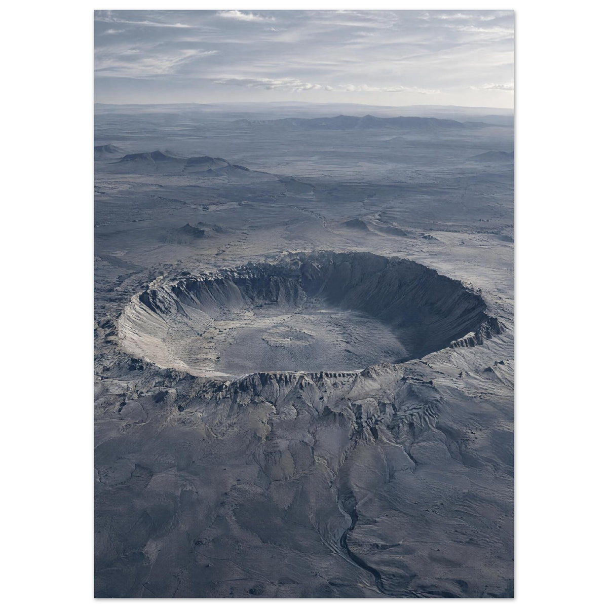 Large circular crater in a blue-grey desert plain, with rugged slopes, distant hills and a cloudy sky.